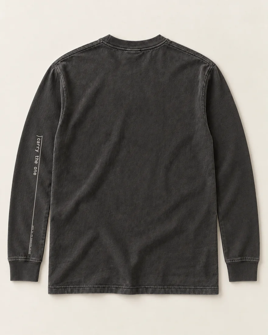 The back of a washed black long-sleeve tee: down the left sleeve, the division bracket and carry the one, a thin bar running to the cuff, the motto small at its end.